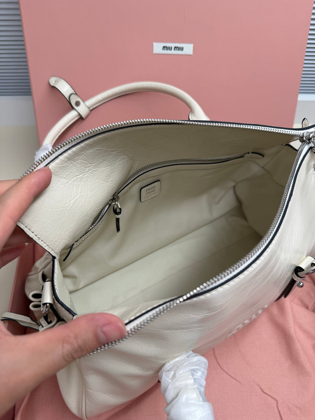 White leather handbag open view with zip top, fabric lining, and inner pocket