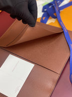 Louis Vuitton brown leather card holder with interior pocket, held by gloved hand.