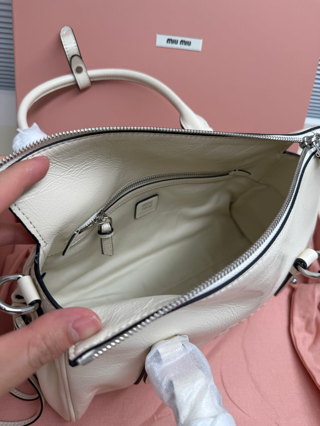 White leather bag interior view with zipper pocket and logo patch at top
