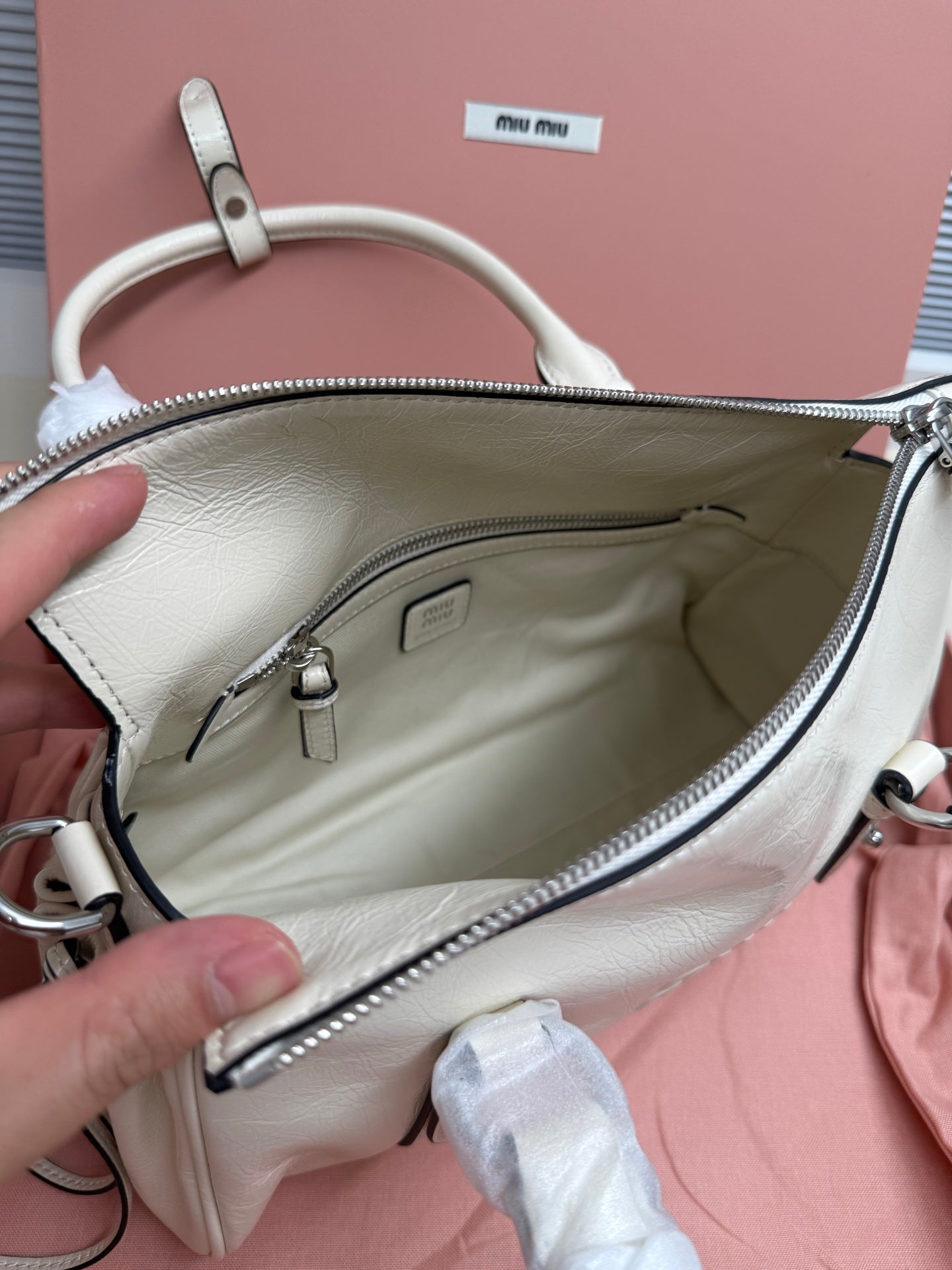 White leather bag interior view with zipper pocket and logo patch at top
