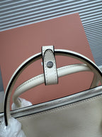 White leather bag top handle close-up with stitched tab and metal rivet