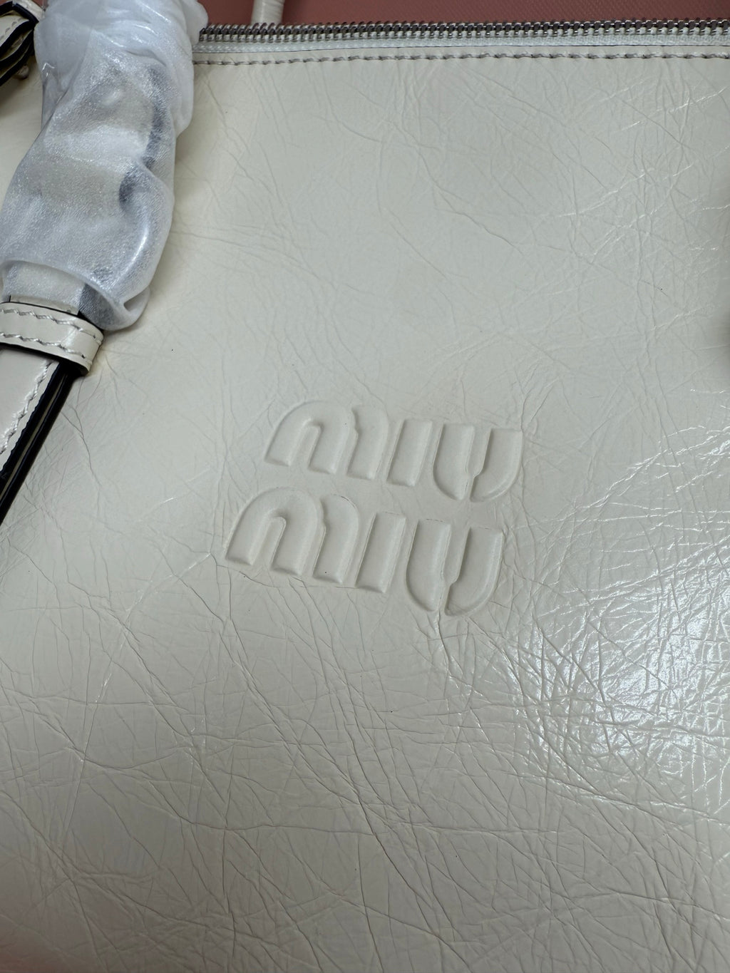 White leather bag close-up with embossed miu miu logo and stitched edge zipper