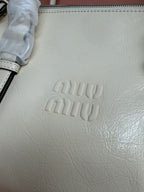 White leather bag close-up with embossed miu miu logo and stitched edge zipper
