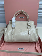 Light green leather handbag with zip top, dual handles, front logo plaque and buckles