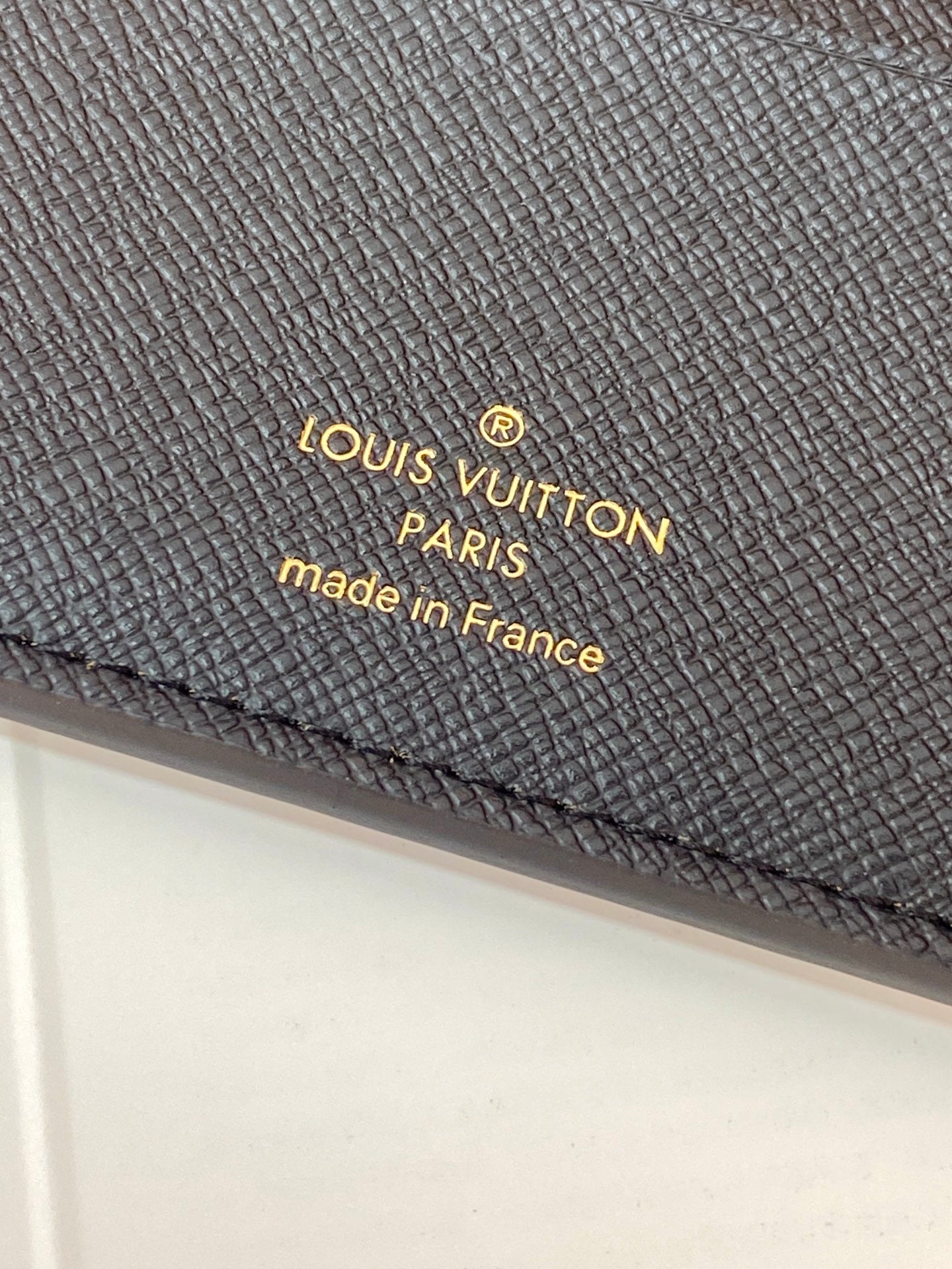 Louis Vuitton small bag close-up: embossed 'LV Paris' on dark textured leather.