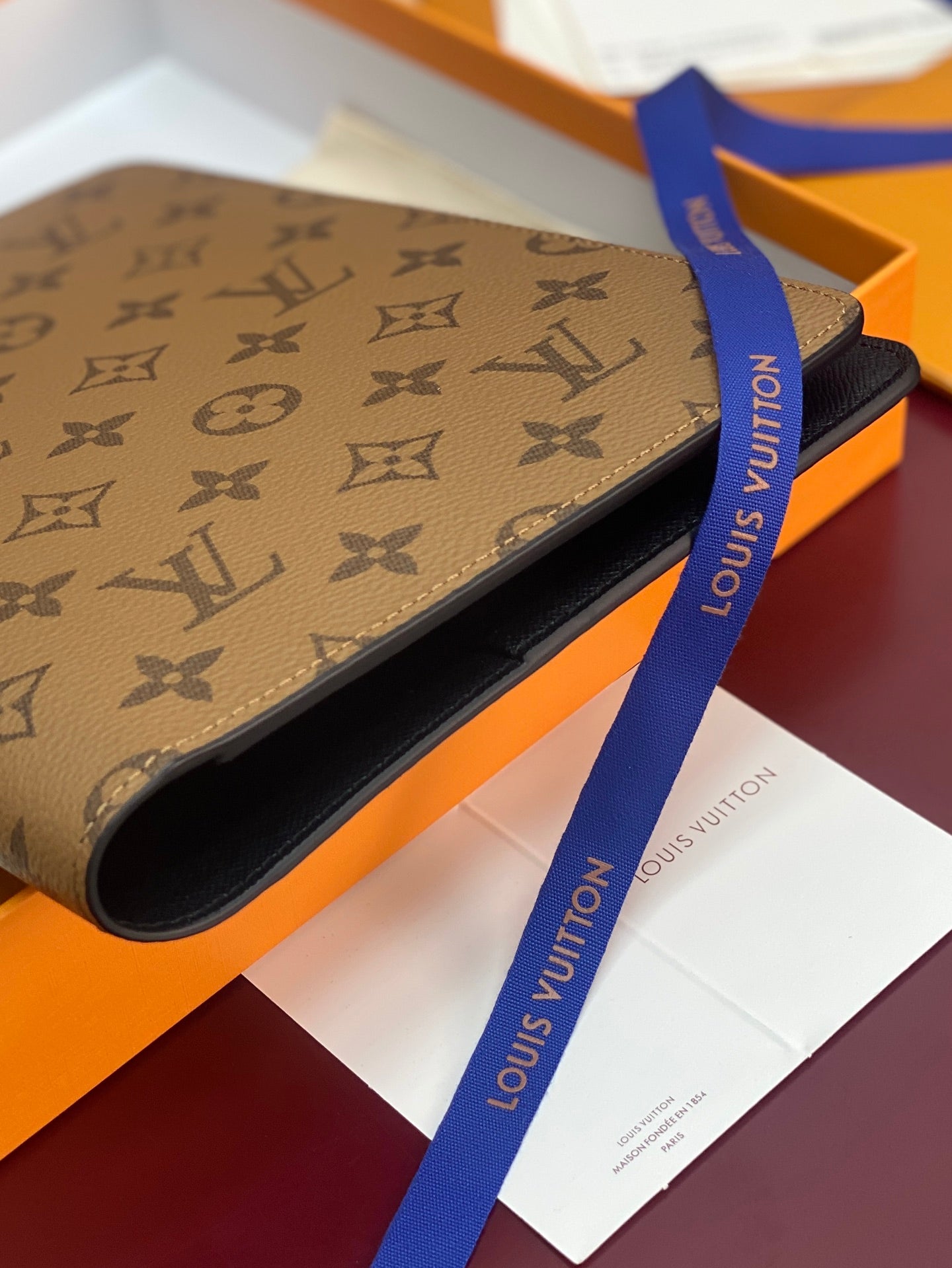 Louis Vuitton small bag in tan monogram canvas with navy ribbon and open edge.