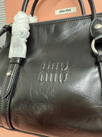 Dark leather handbag front panel with debossed logo and side strap hardware.