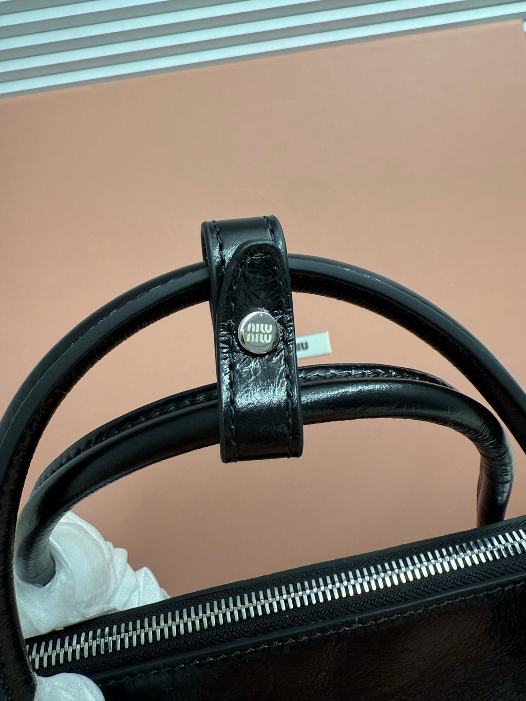Dark leather handbag handle attachment with stitched trim and zipper top edge.
