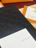 Close-up of black embossed monogram leather wallet surface detail.
