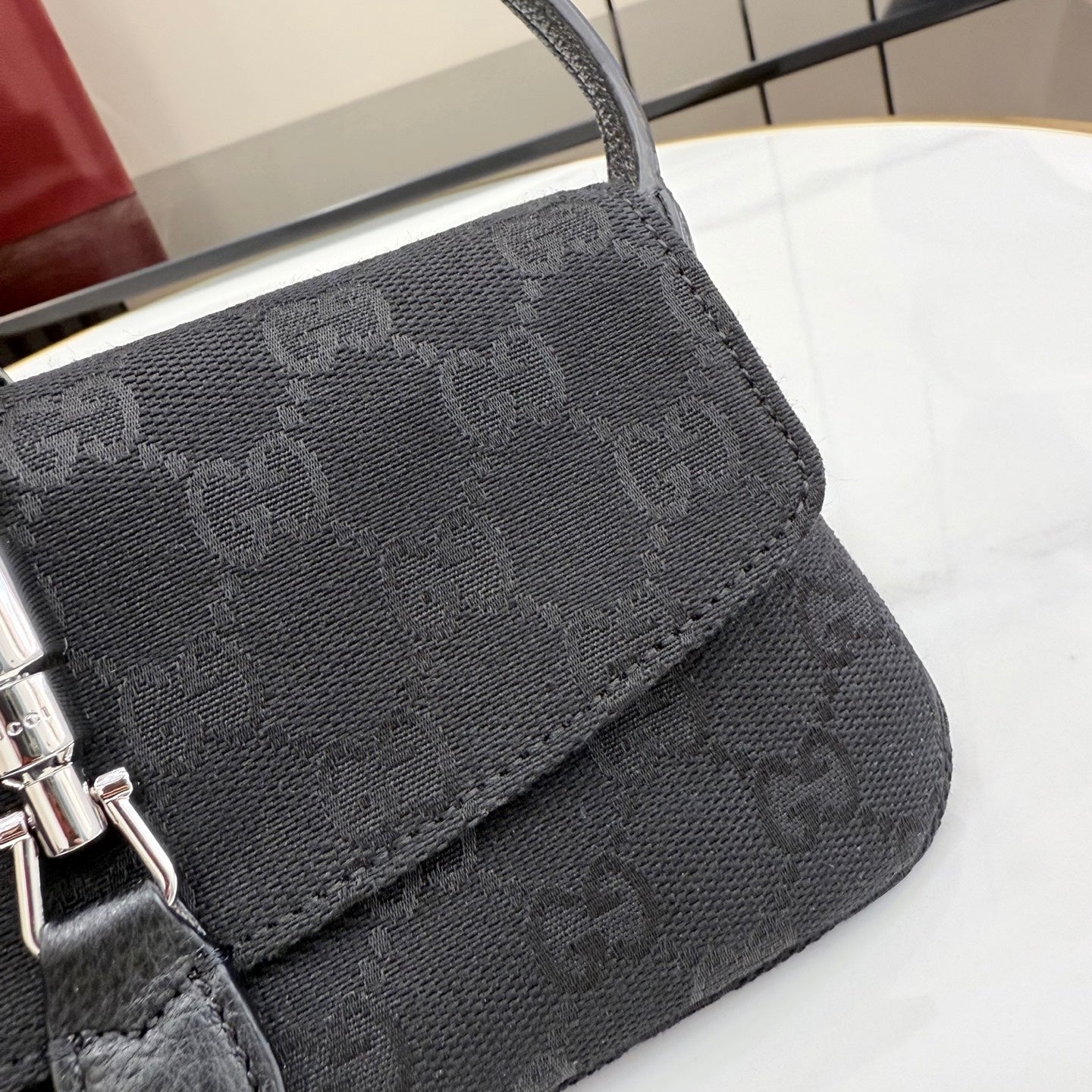 Gray Gucci crossbody bag corner with monogram texture and stitched trim near flap.