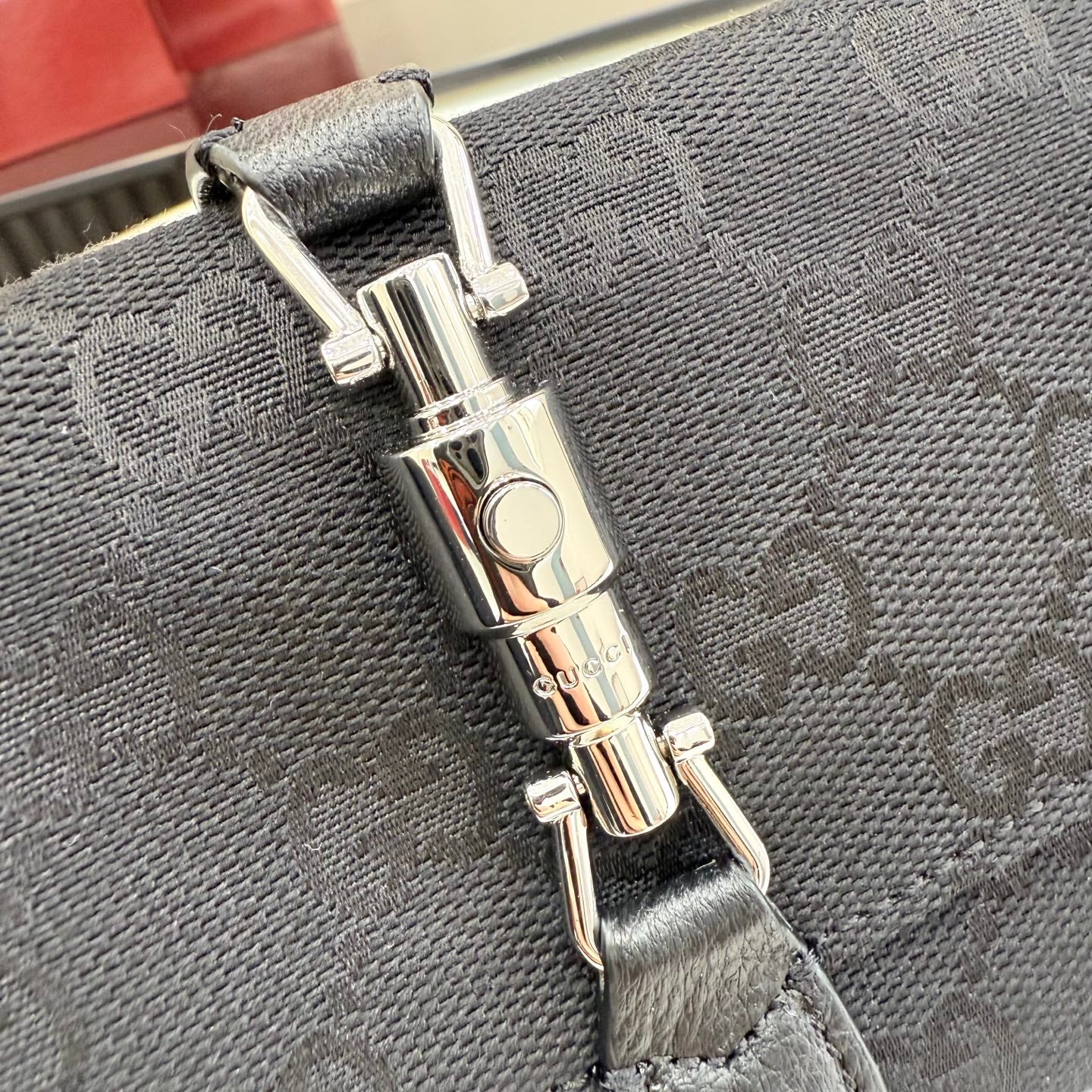 Close-up of silver-tone turn-lock clasp and strap attachment on a gray monogram bag.