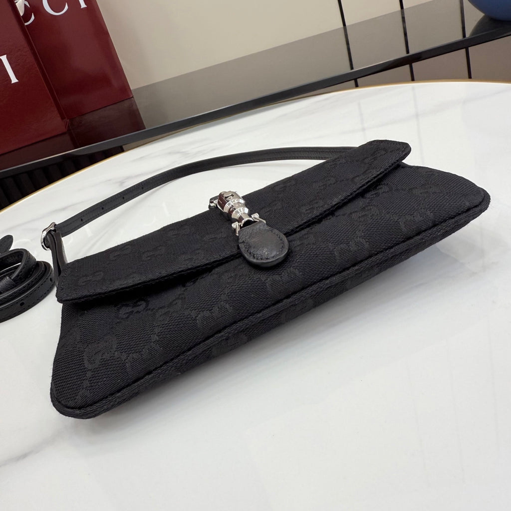 Black Gucci clutch-style bag with long strap, monogram texture, and silver clasp closure.