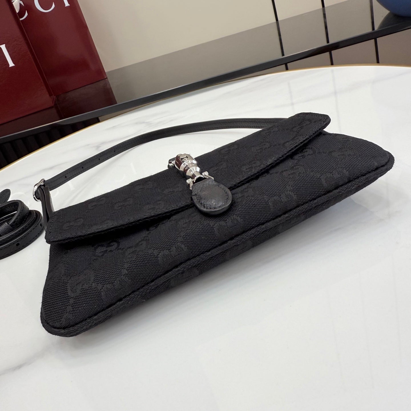 Black Gucci clutch-style bag with long strap, monogram texture, and silver clasp closure.