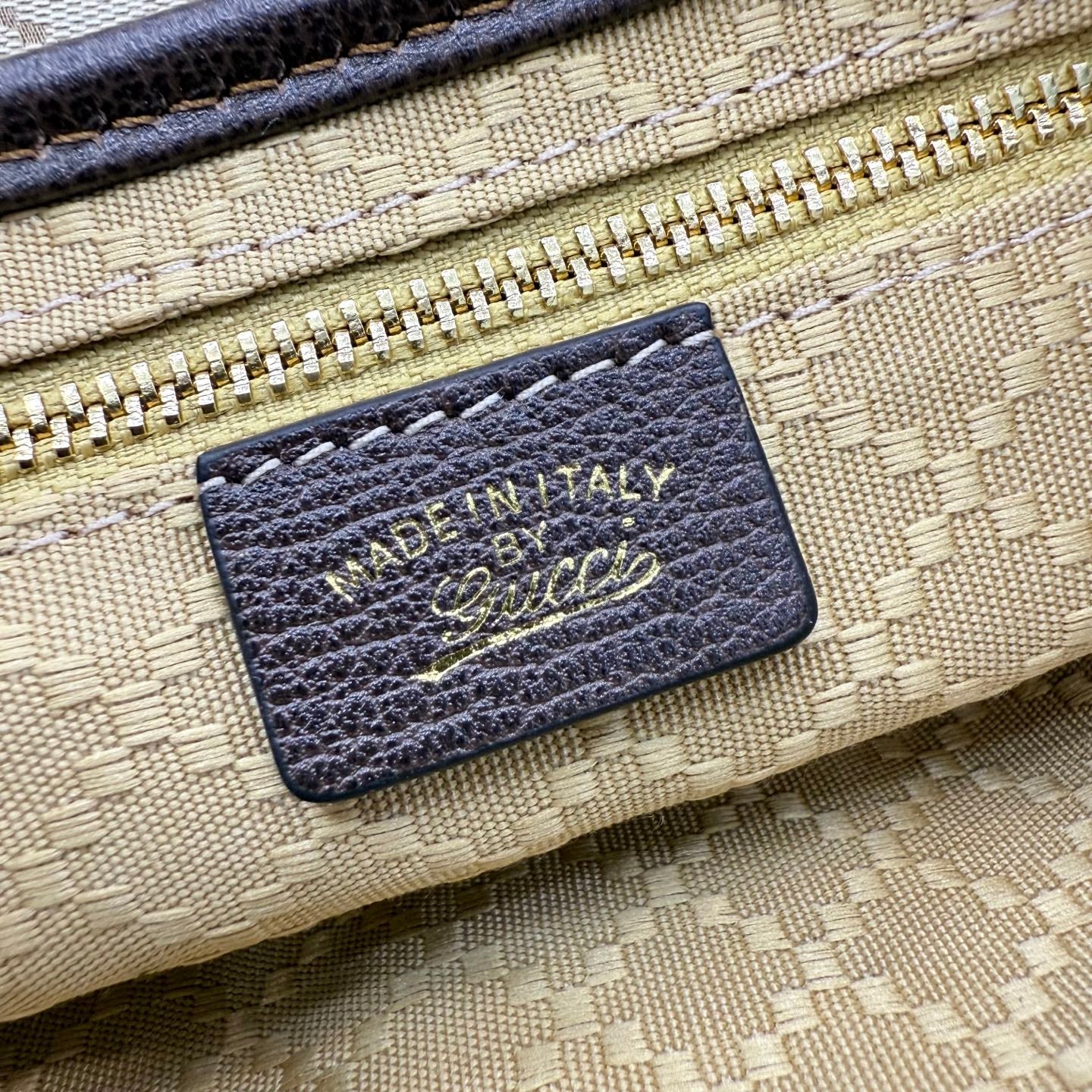 Beige bag leather label with dark border, showing Made in Italy and signature-style logo