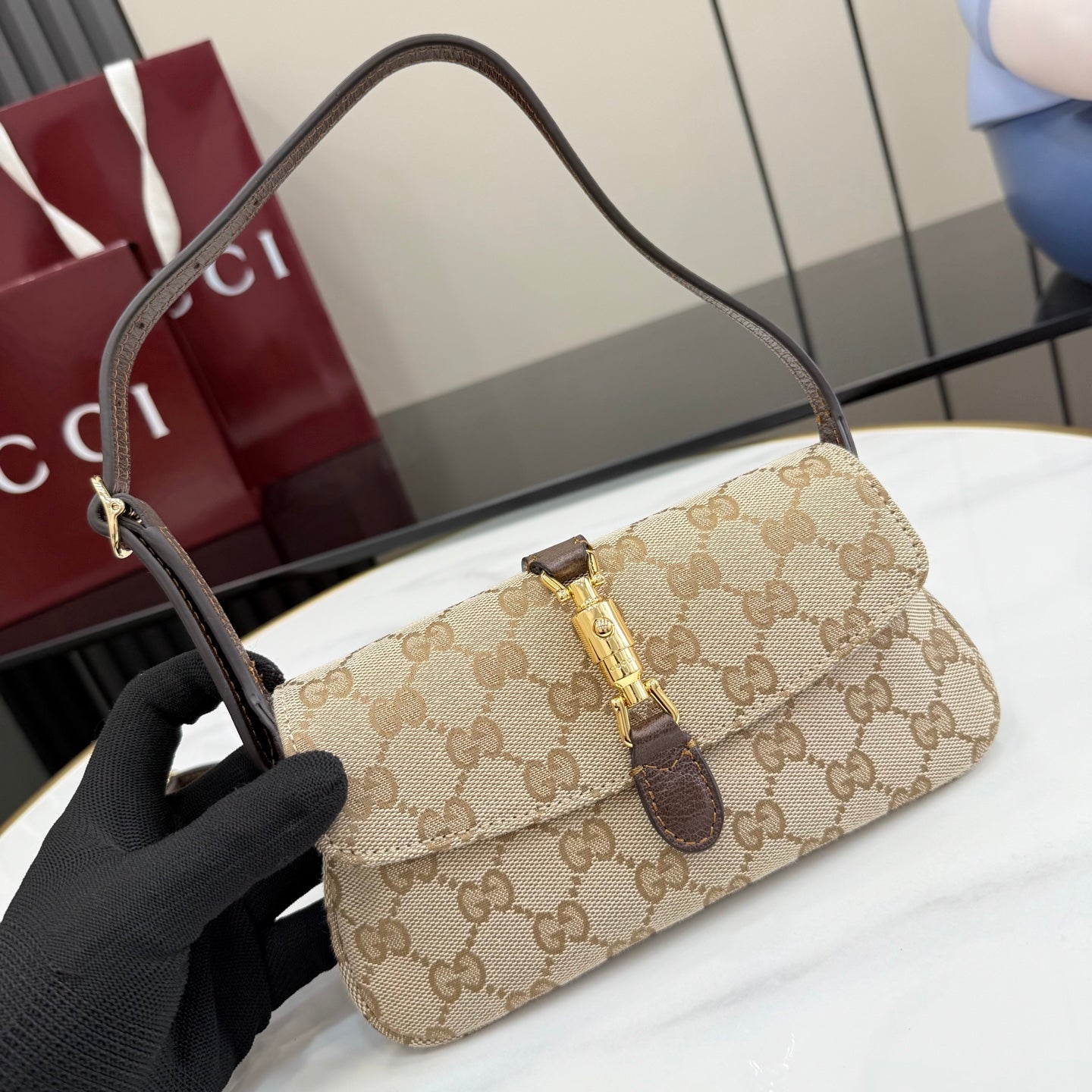 Beige GG-pattern shoulder bag with dark brown top strap, gold clasp, and flap closure