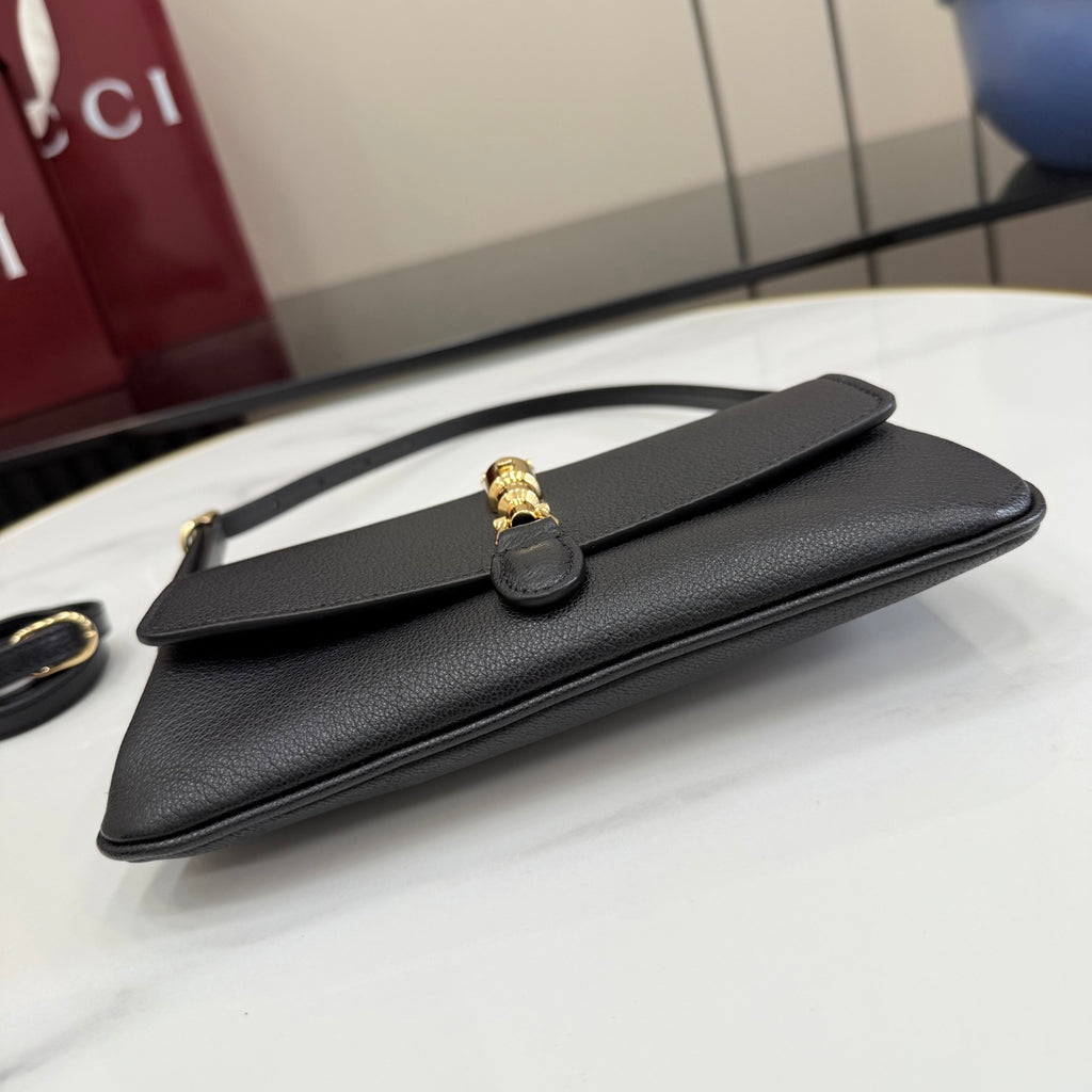 Black Gucci shoulder bag with top handle and flap, gold clasp on front, flat lay