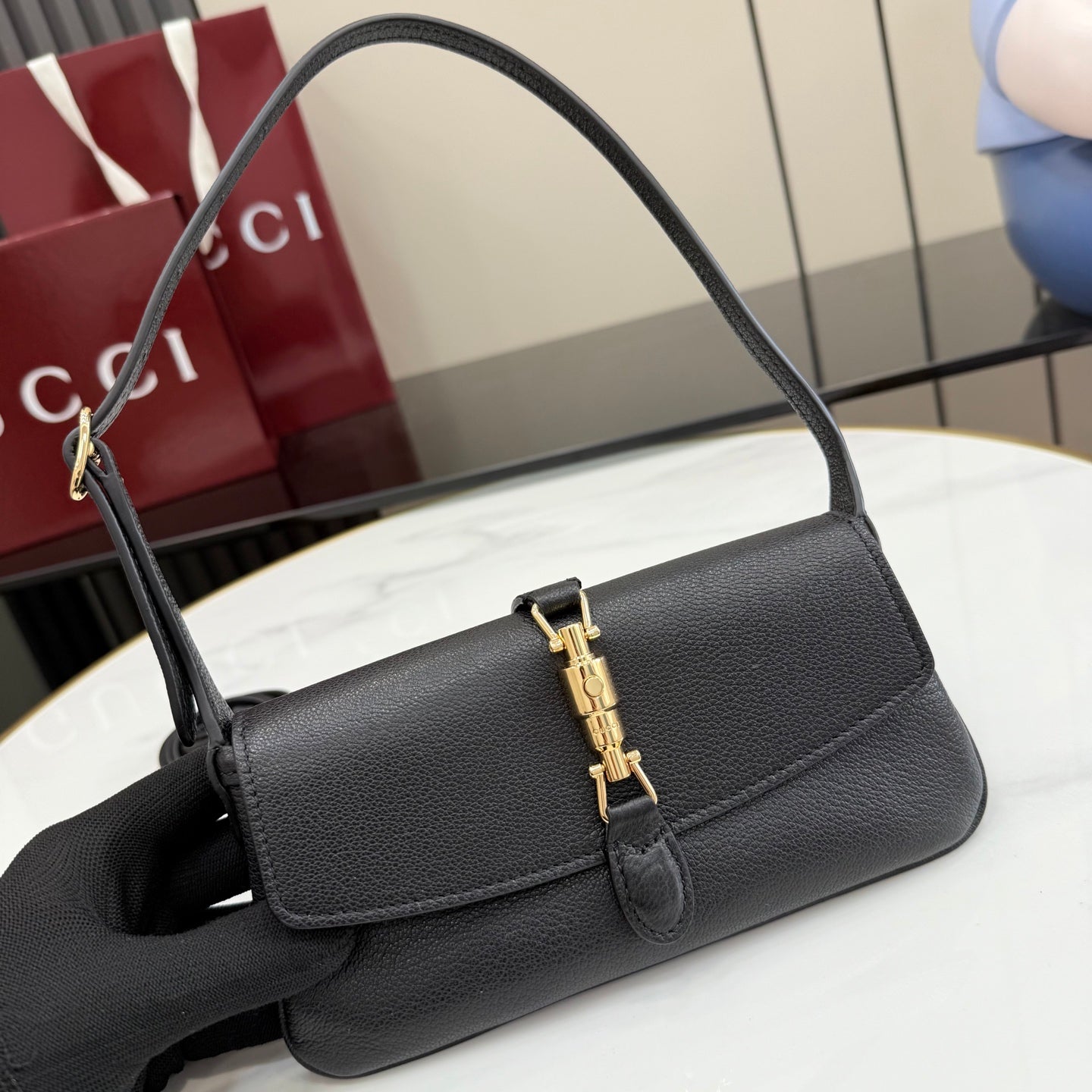 Black Gucci shoulder bag with curved top handle and gold clasp on flap front