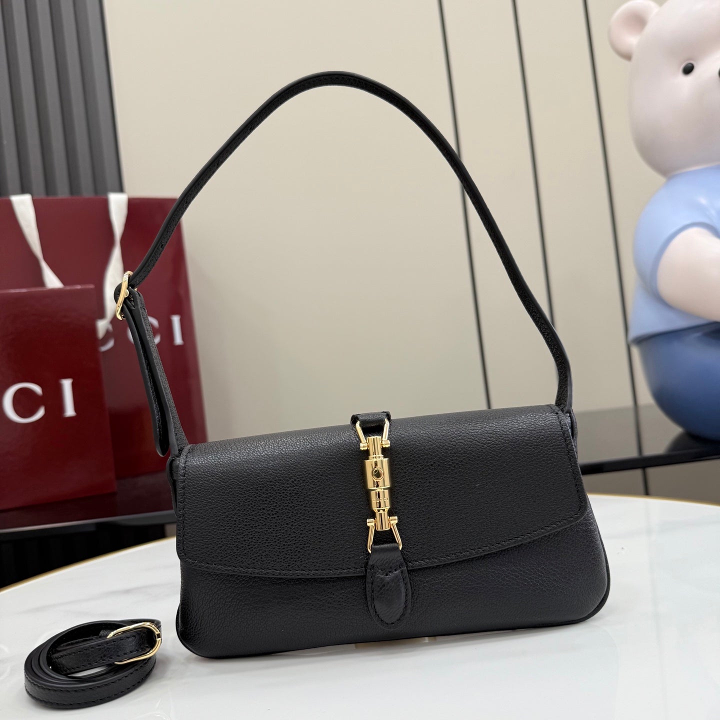 Black Gucci shoulder bag with top handle, flap front, and gold clasp hardware
