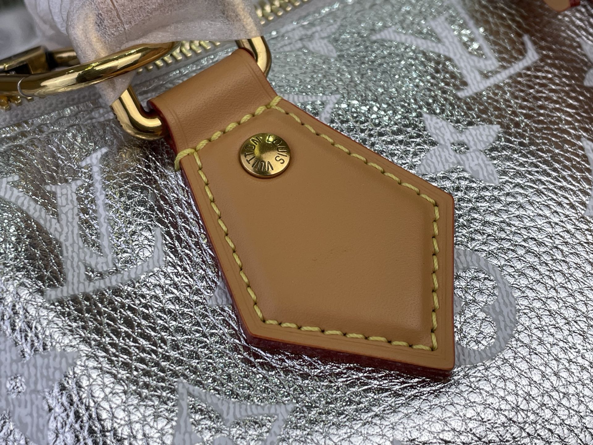 Tan leather luggage tag with Louis Vuitton stamp and yellow stitching on silver canvas