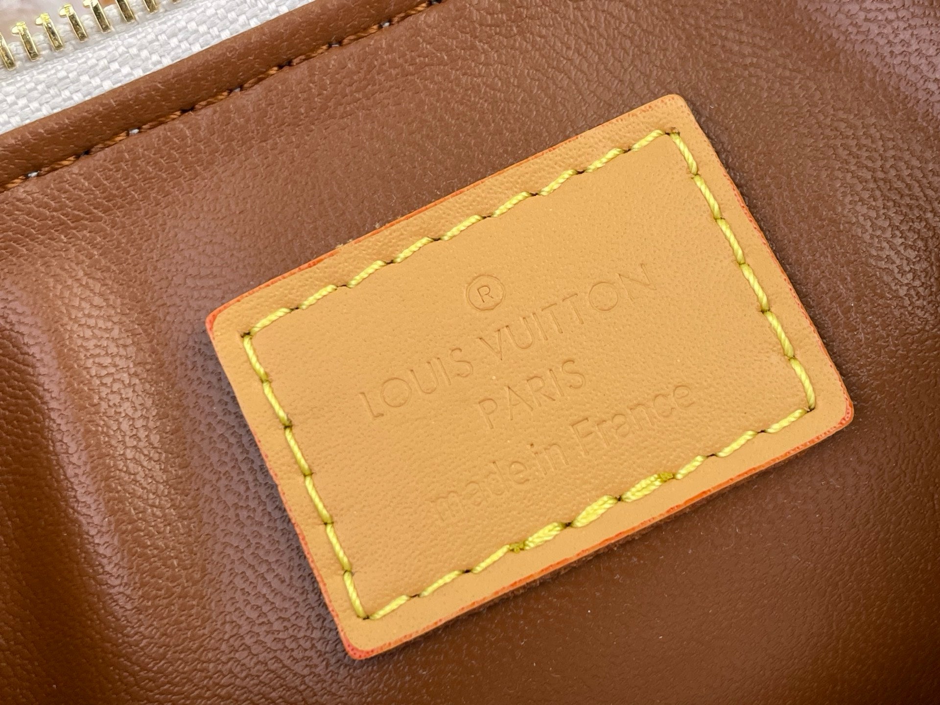 Brown leather luggage tag with yellow-stitched frame and Louis Vuitton logo