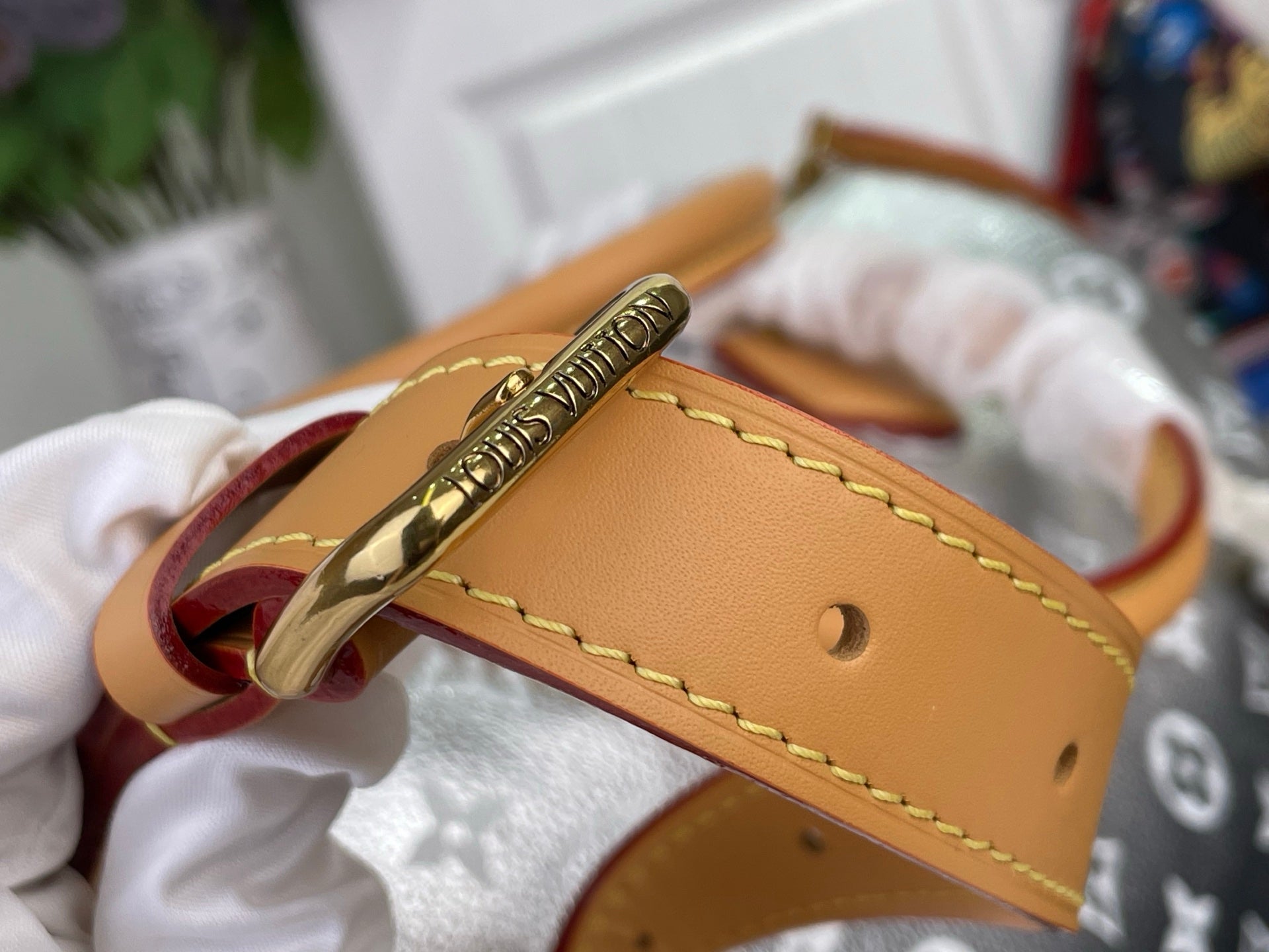 Tan leather wrist strap with gold clasp and stitching on monogram canvas bag