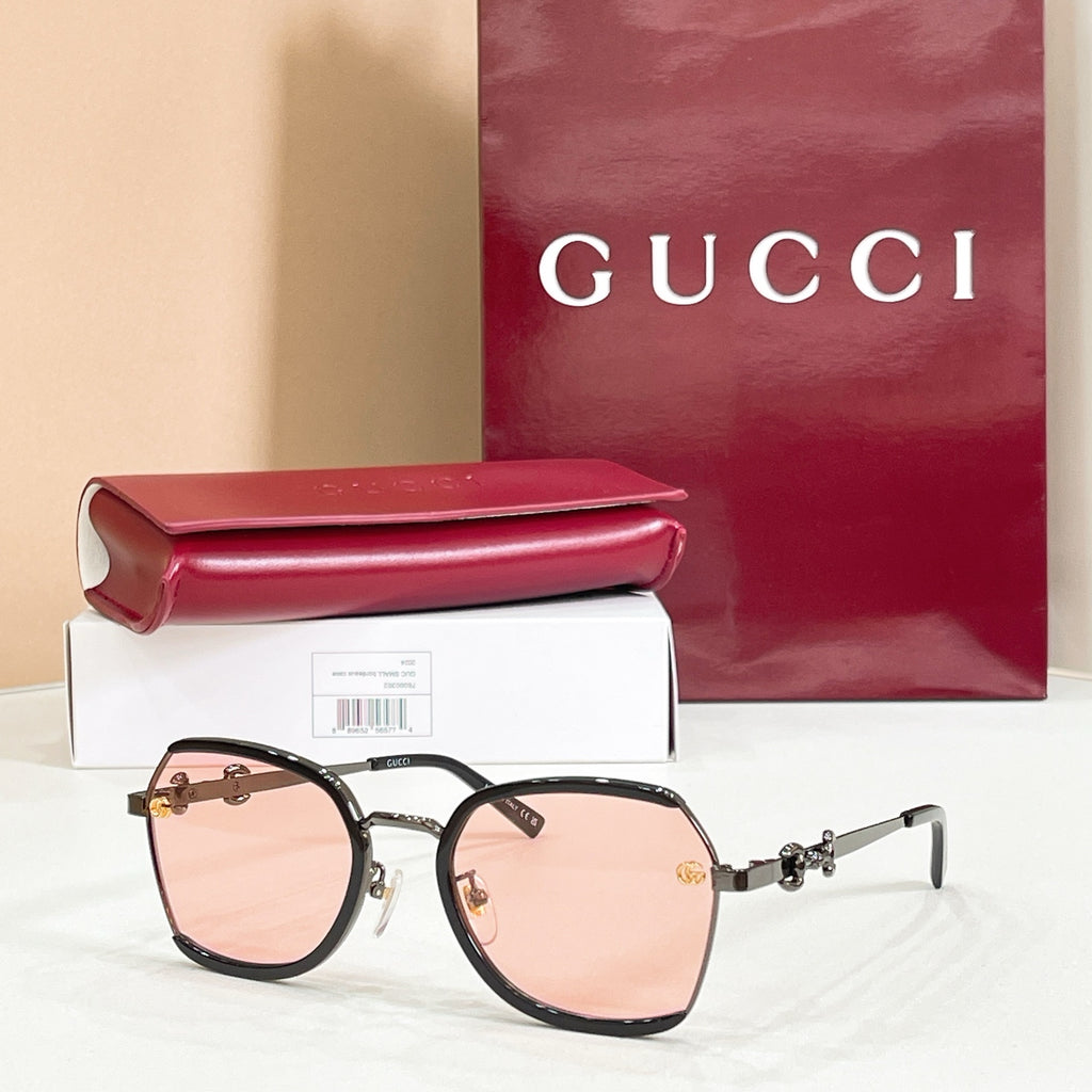 Black round sunglasses with blush-pink lenses and gold logo hinges.