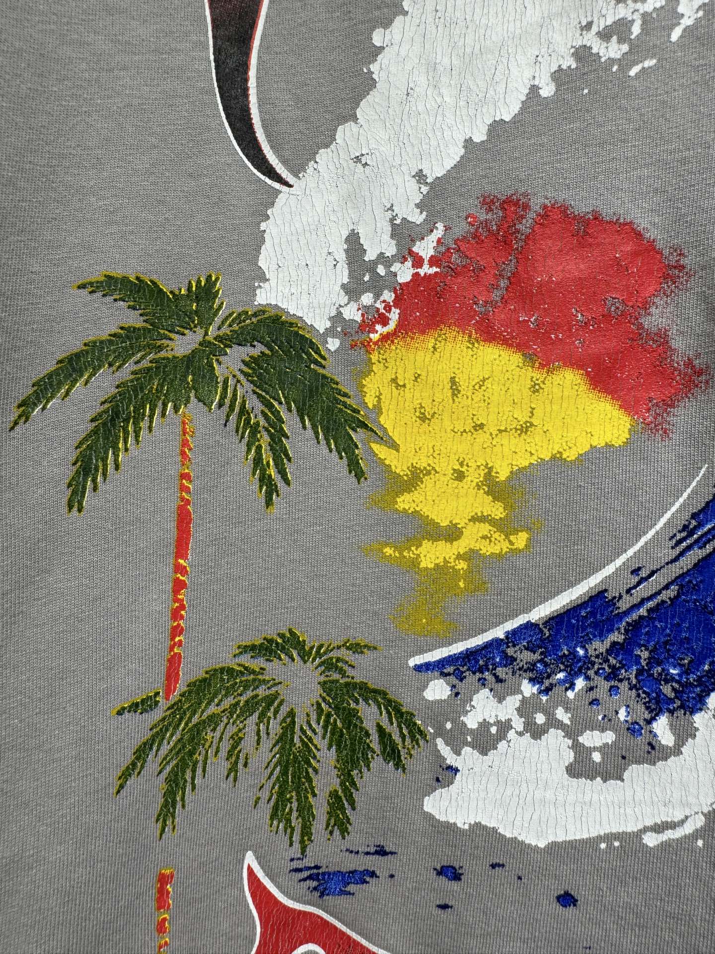 Light gray T-shirt close-up of colorful face graphic with palm tree motifs