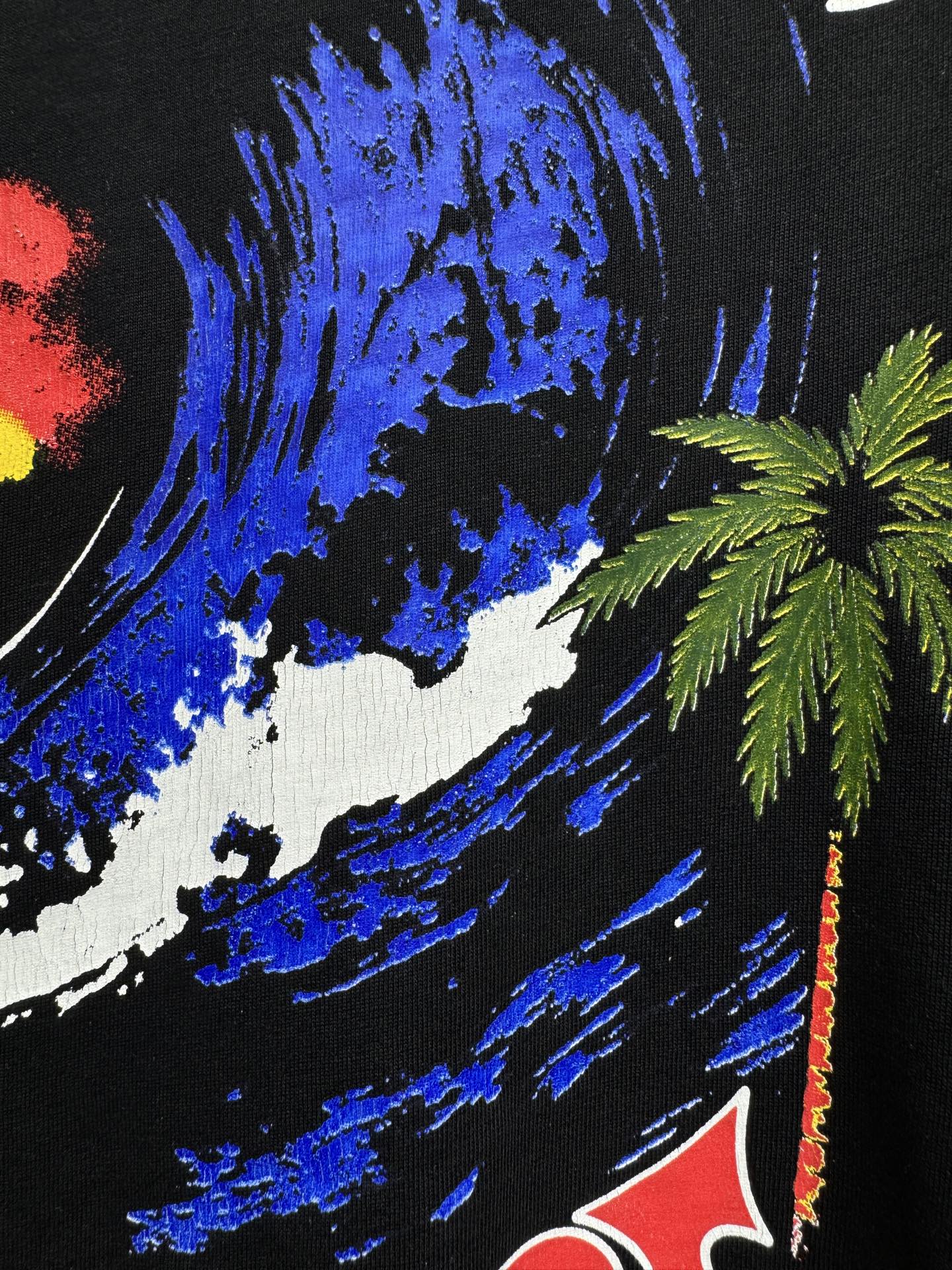Black graphic T-shirt close-up with blue paint strokes and palm tree detail