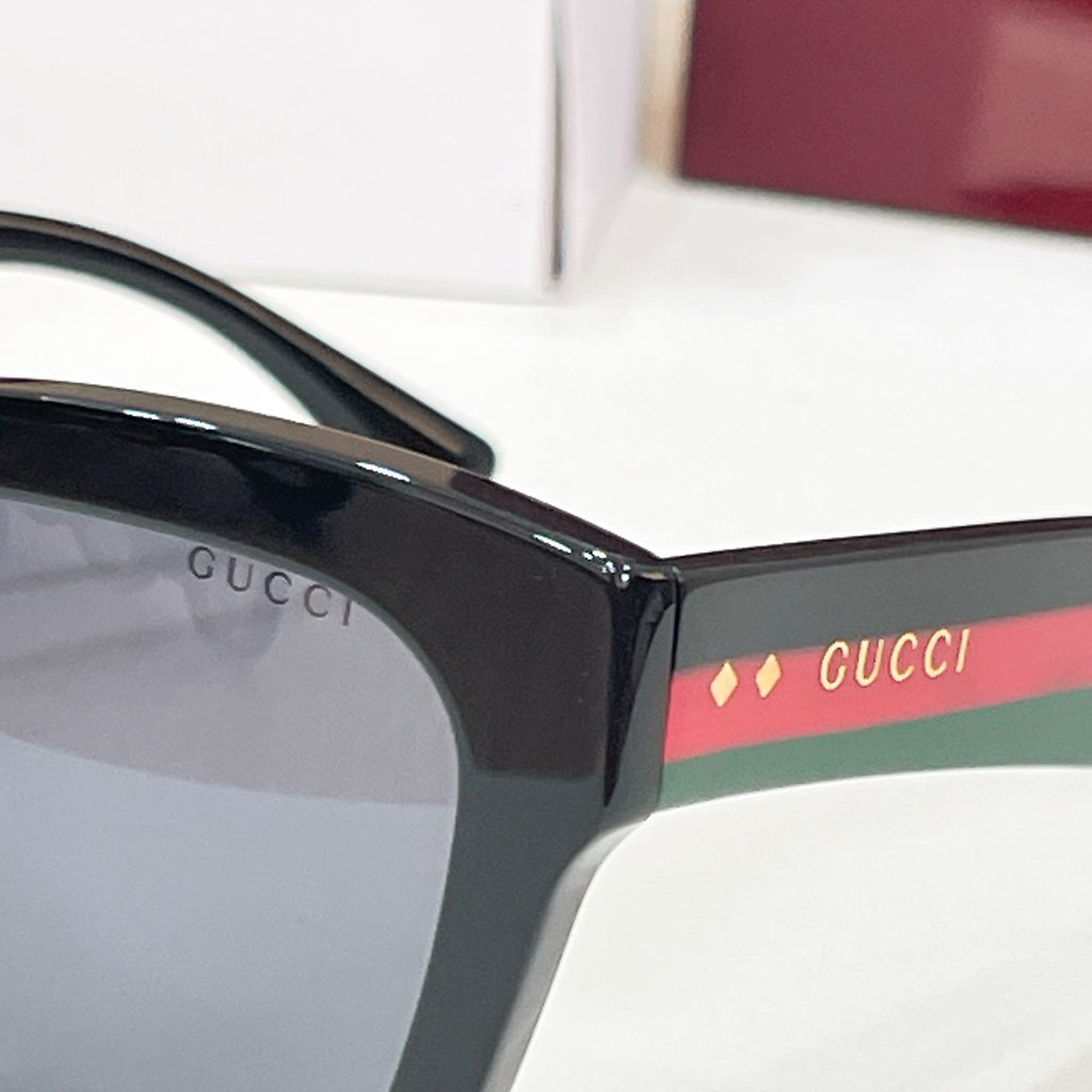 Black square eyeglass frame close-up with Gucci logo on the lens rim.