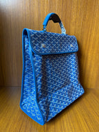Blue patterned tote-style handbag with flap and top handle, side view, gold-tone