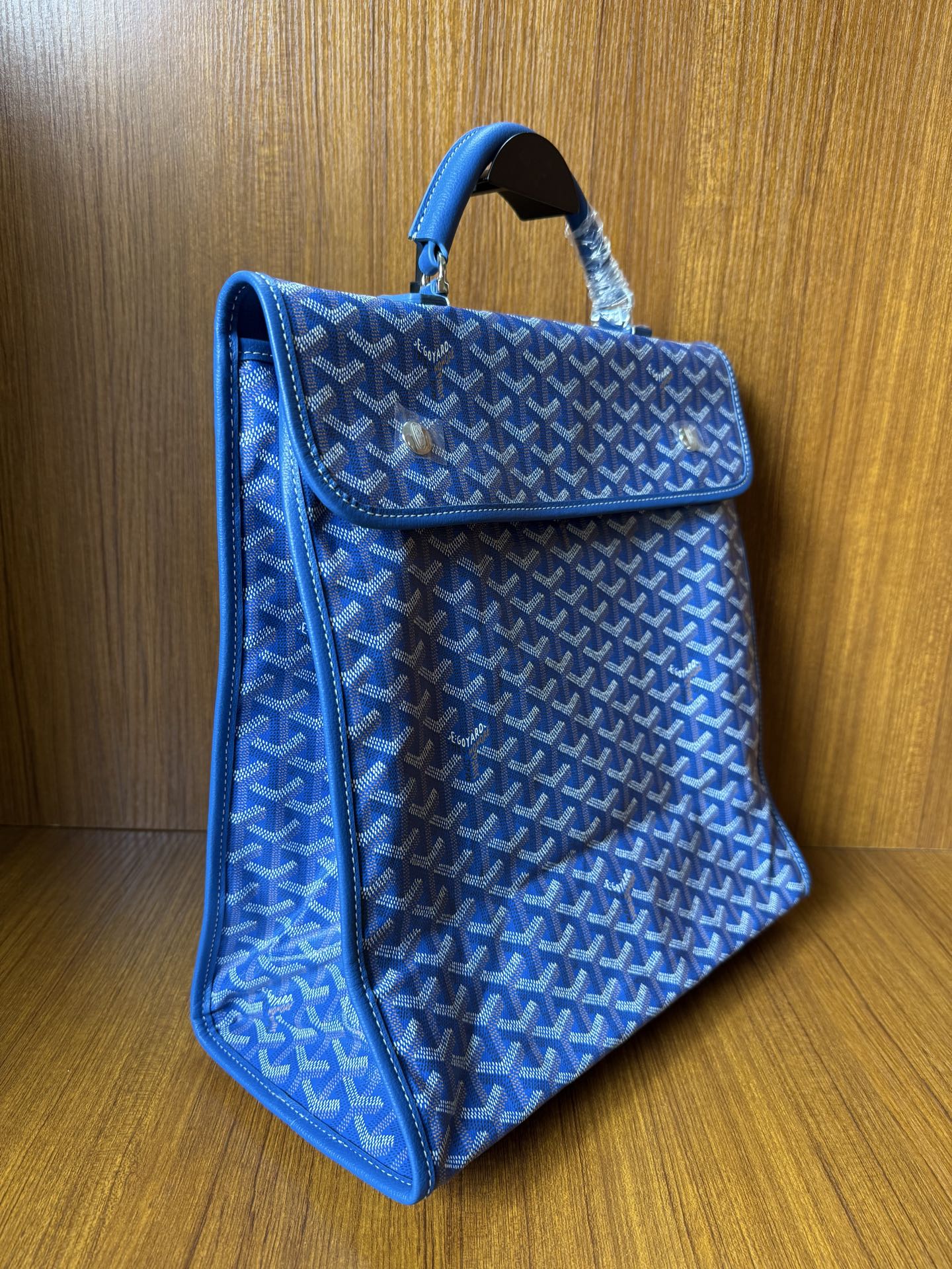 Blue patterned tote-style handbag with flap and top handle, side view, gold-tone
