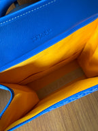 Orange-lined interior of a blue handbag with stitched seam along inner wall