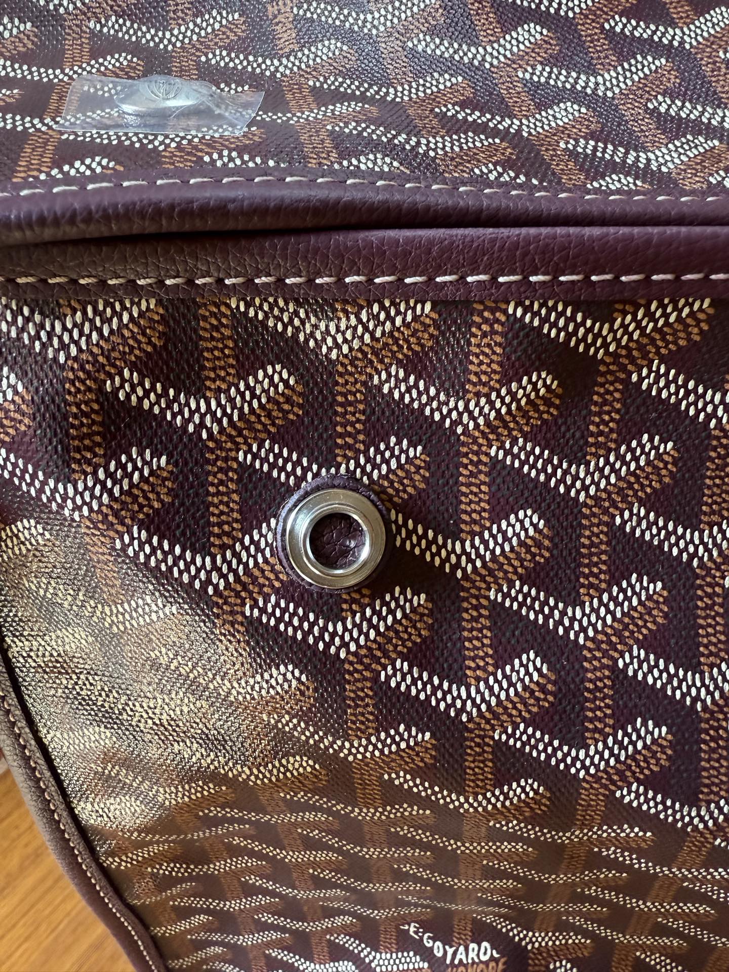 Goyard monogram tote bag side with round metal rivet and small leather brand tag