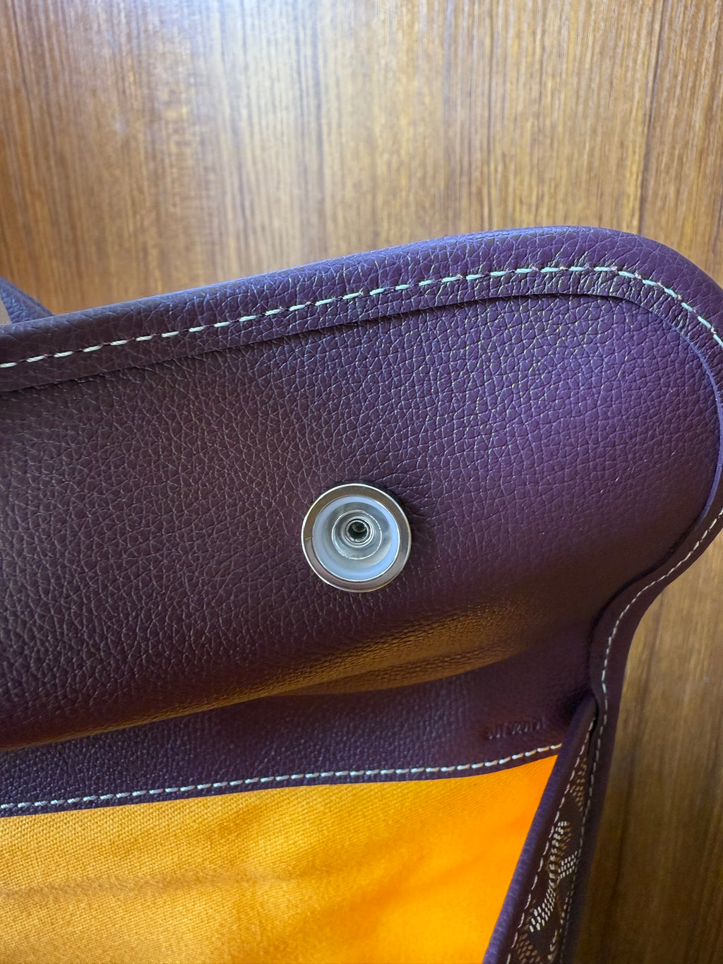 Goyard leather handle end with round metal snap and stitched trim on monogram bag