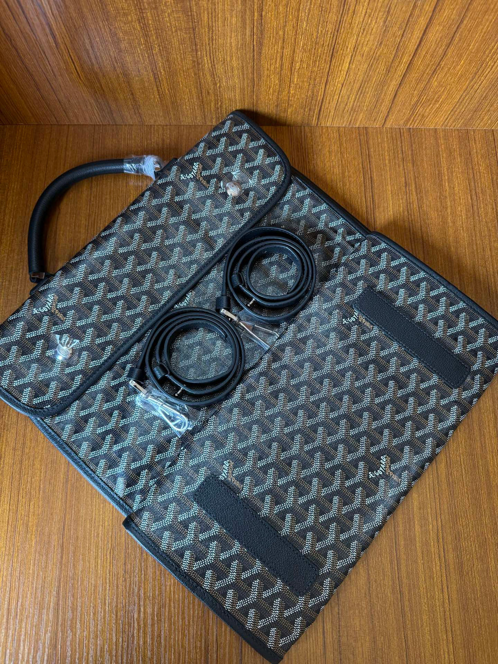 Goyardine patterned bag with open flap and two round items inside, dark blue-gray.