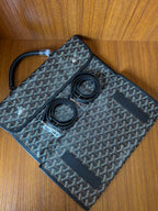 Goyardine patterned bag with open flap and two round items inside, dark blue-gray.