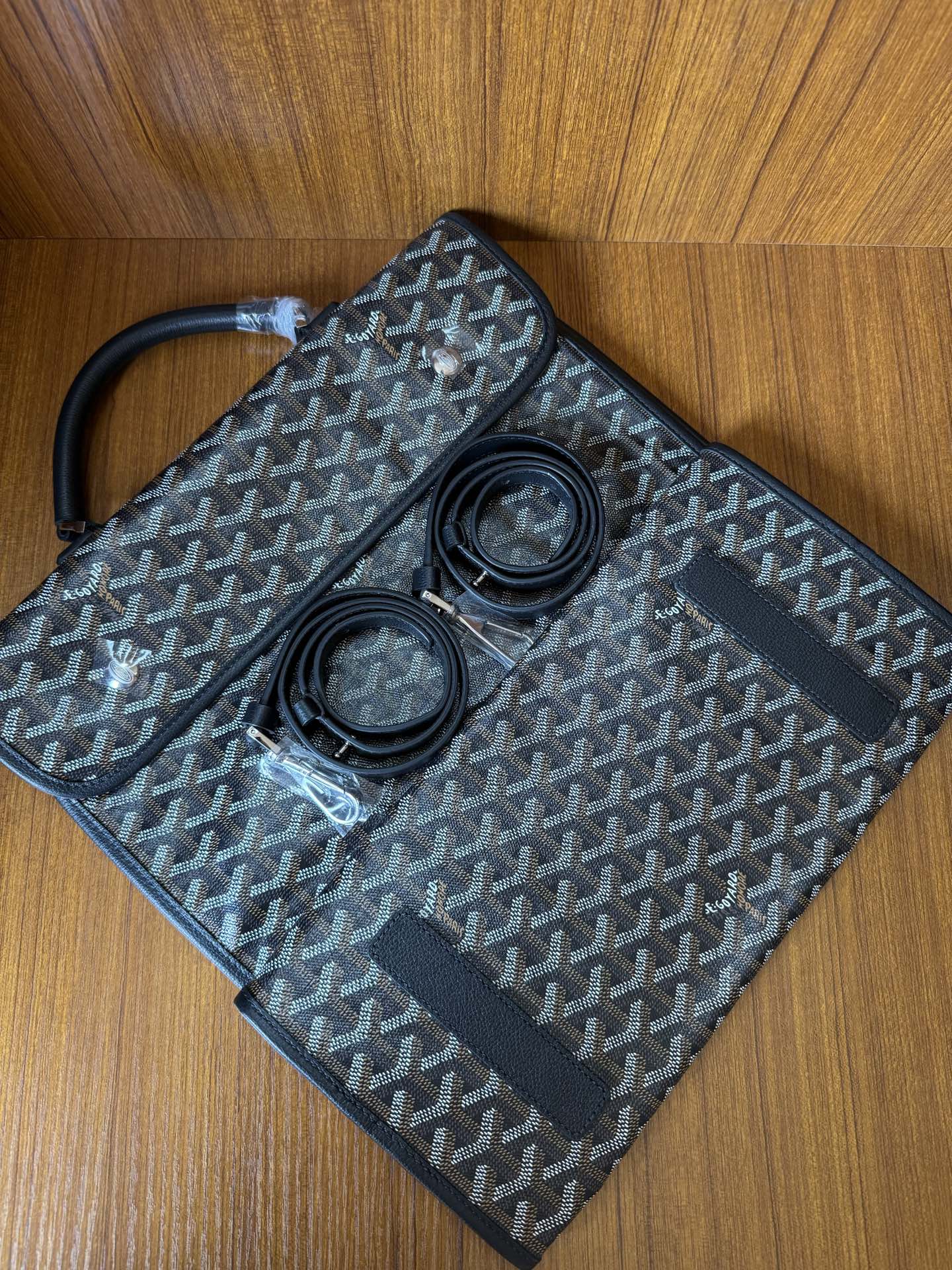 Goyardine patterned bag with open flap and two round items inside, dark blue-gray.