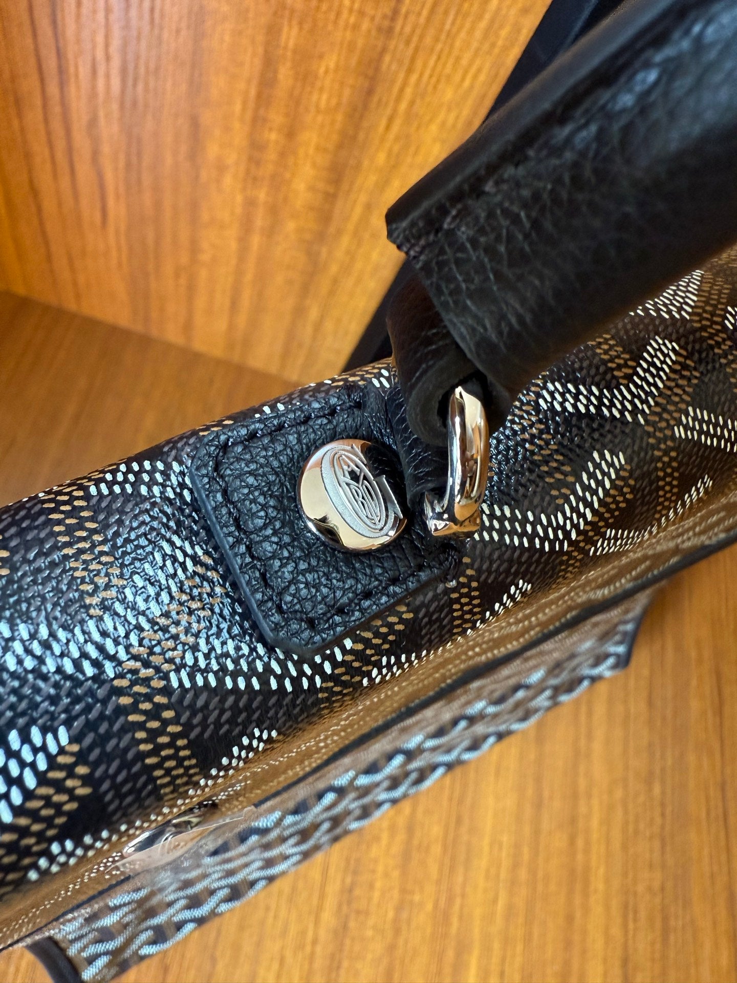 Close-up of clasp hardware and trim on Goyardine patterned bag, dark blue-gray.