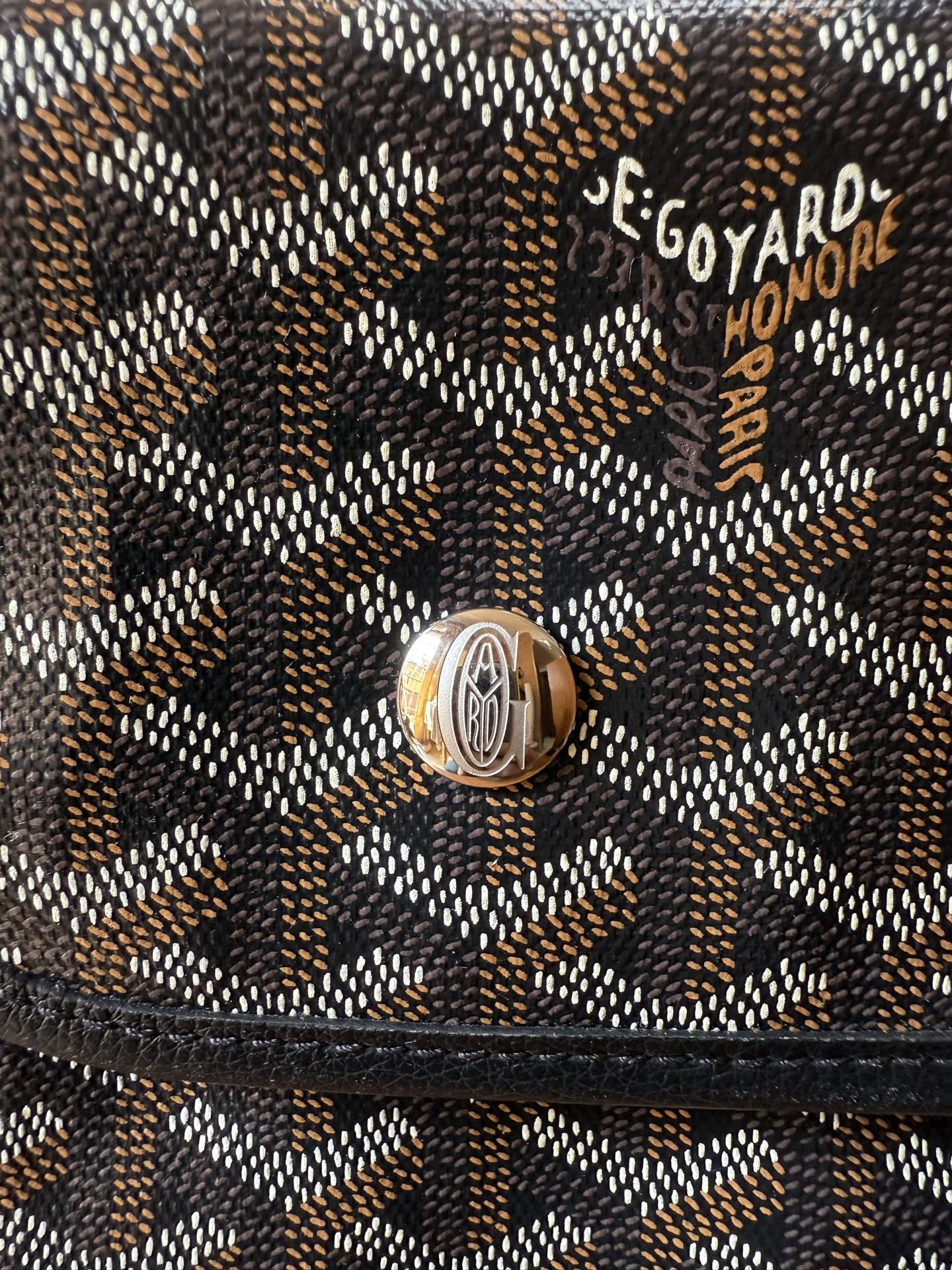 Logo patch on Goyardine patterned bag flap with metal snap hardware.