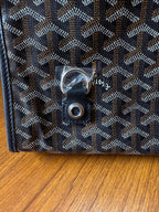 Close-up of snap button and metal hardware on Goyardine bag, dark blue-gray.