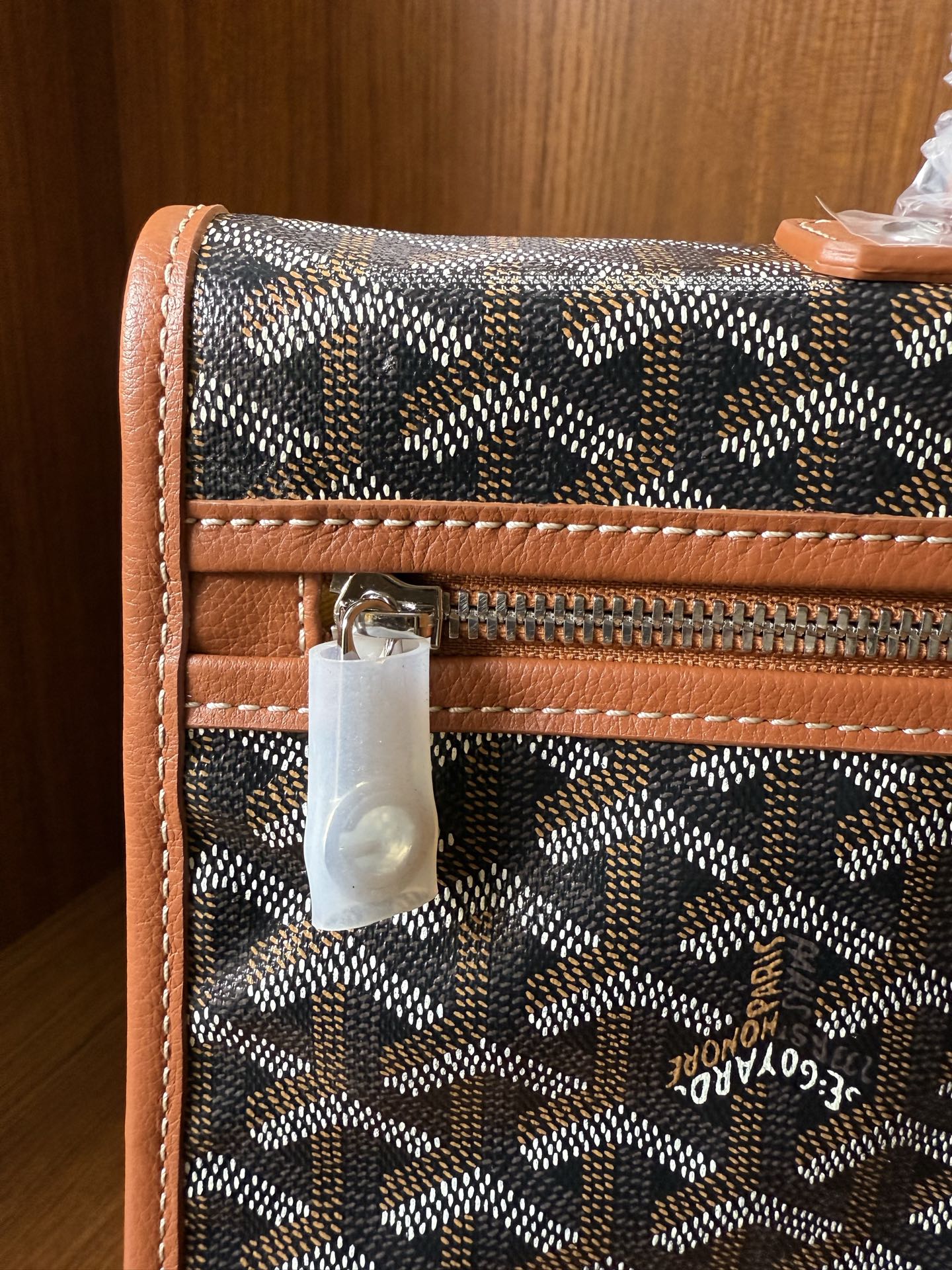 Designer tote bag close-up with Goyard-style pattern, zip pocket, tan leather edging