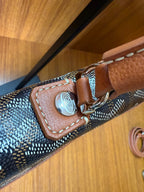 Designer tote bag corner with Goyard-style pattern, tan leather strap and metal snap hardware