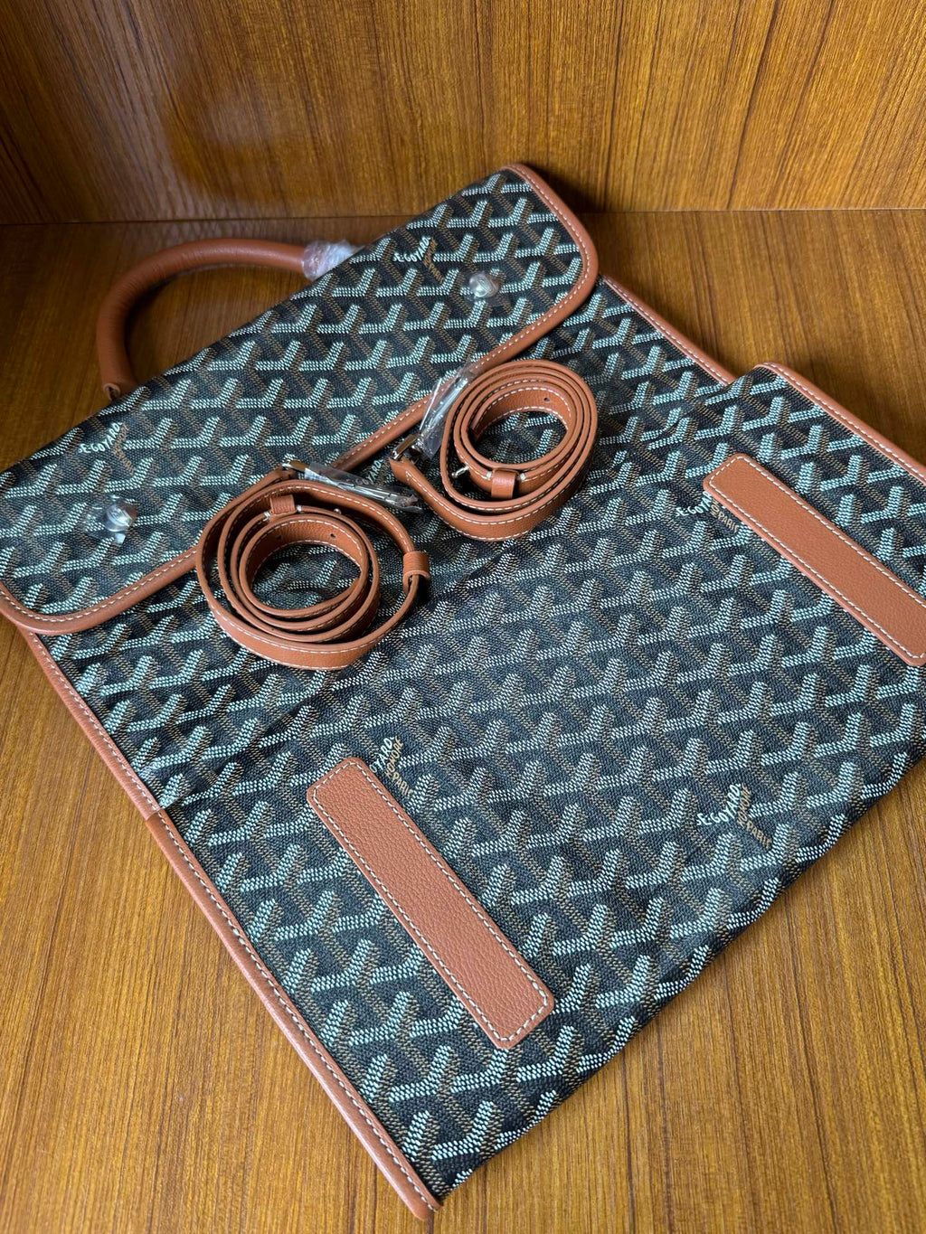 Designer tote bag laid flat with Goyard-style pattern, tan trim, two strap pieces, tag