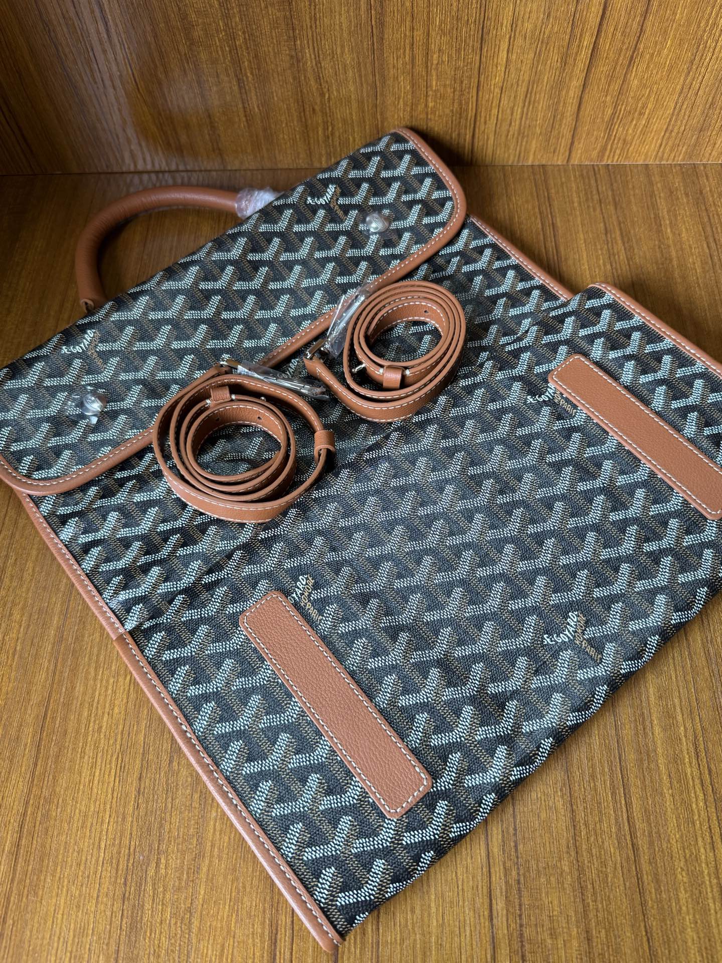 Designer tote bag laid flat with Goyard-style pattern, tan trim, two strap pieces, tag