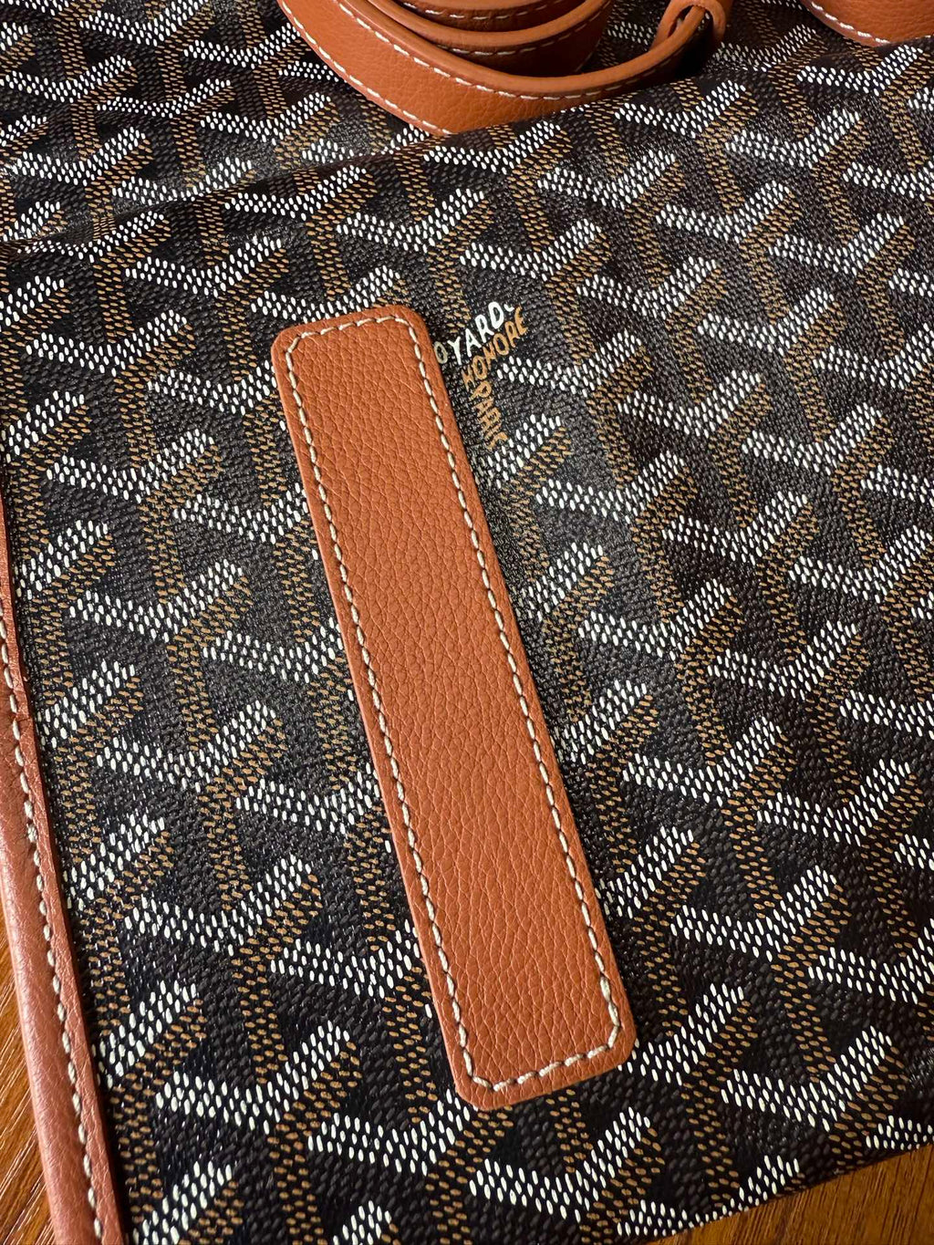 Leather trim panel on designer tote bag with Goyard-style pattern, tan stitched details