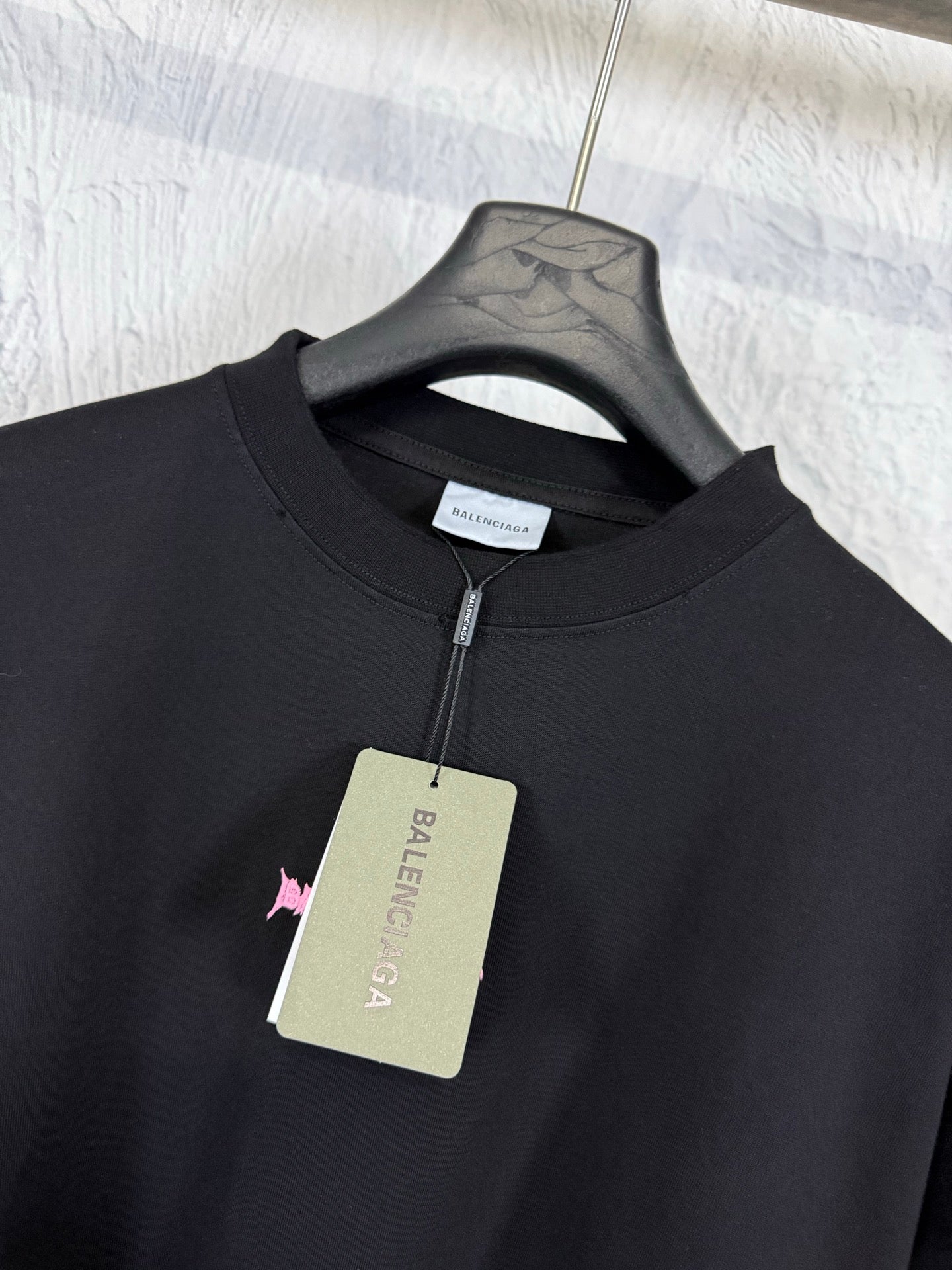Black crew-neck T-shirt on hanger with small Balenciaga logo and hanging tag