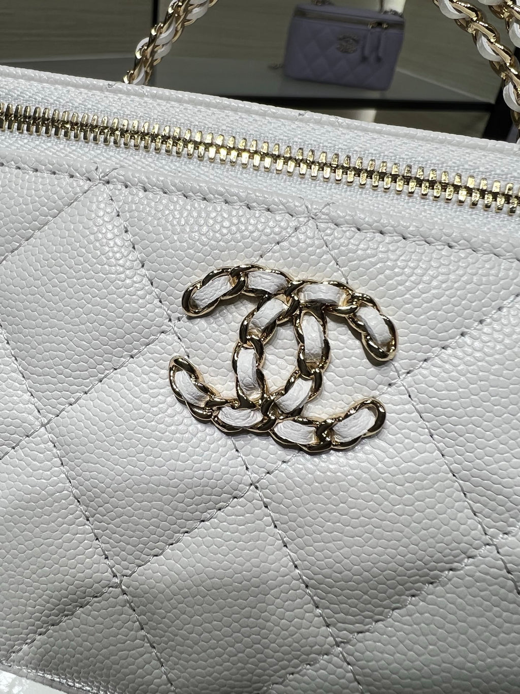 Chanel bag close-up: white textured leather with gold chain zipper pull and hardware.