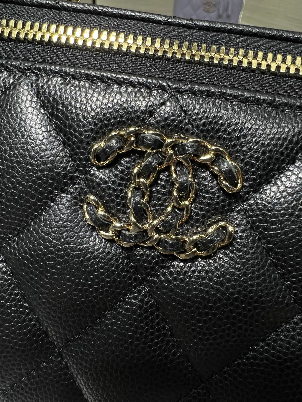 Chanel bag close-up: textured black leather with gold logo charm at front.