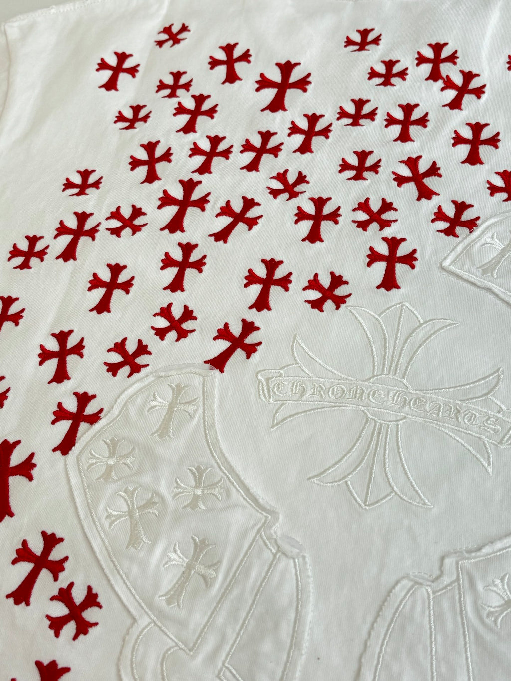 White T-shirt fabric with red cross-style pattern and embossed emblem