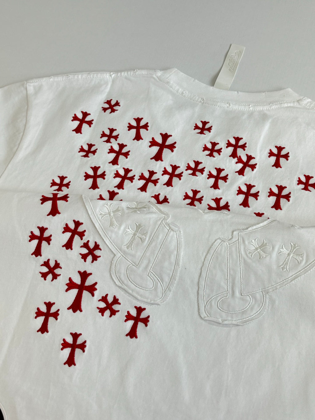 White T-shirt close-up with red pattern and embossed chest emblem detail